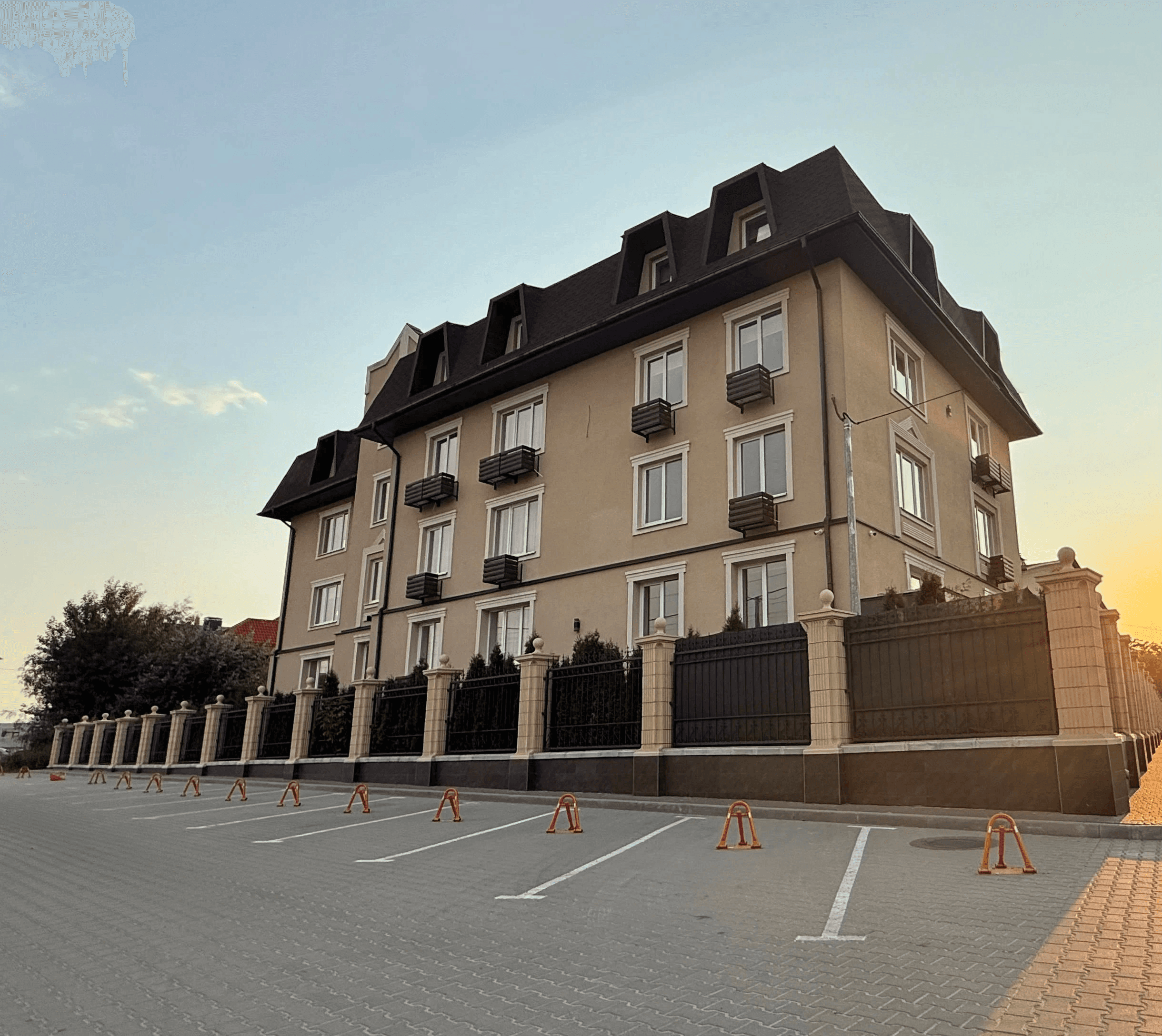 Фасад чотириповерхового будинку з декоративними балконами, високим дахом і огородженою територією