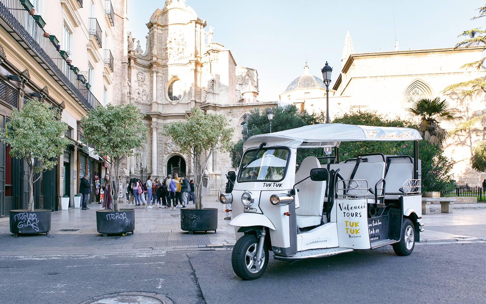 Tuk Tuk parked near Valencia Cathedral, Spain, with tourists nearby.
