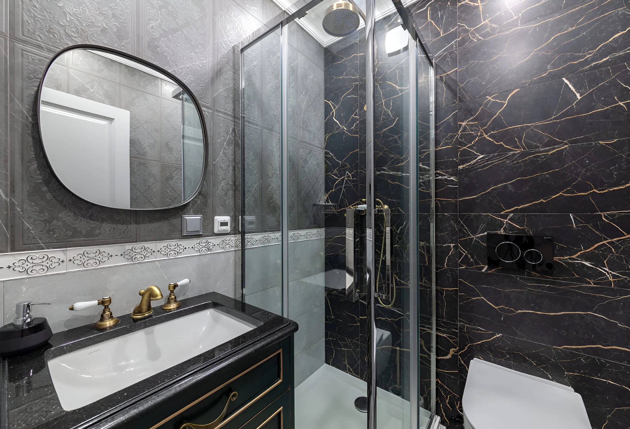 Salle de bain moderne avec parois en marbre noir, robinetterie dorée et douche à l'italienne vitrée.