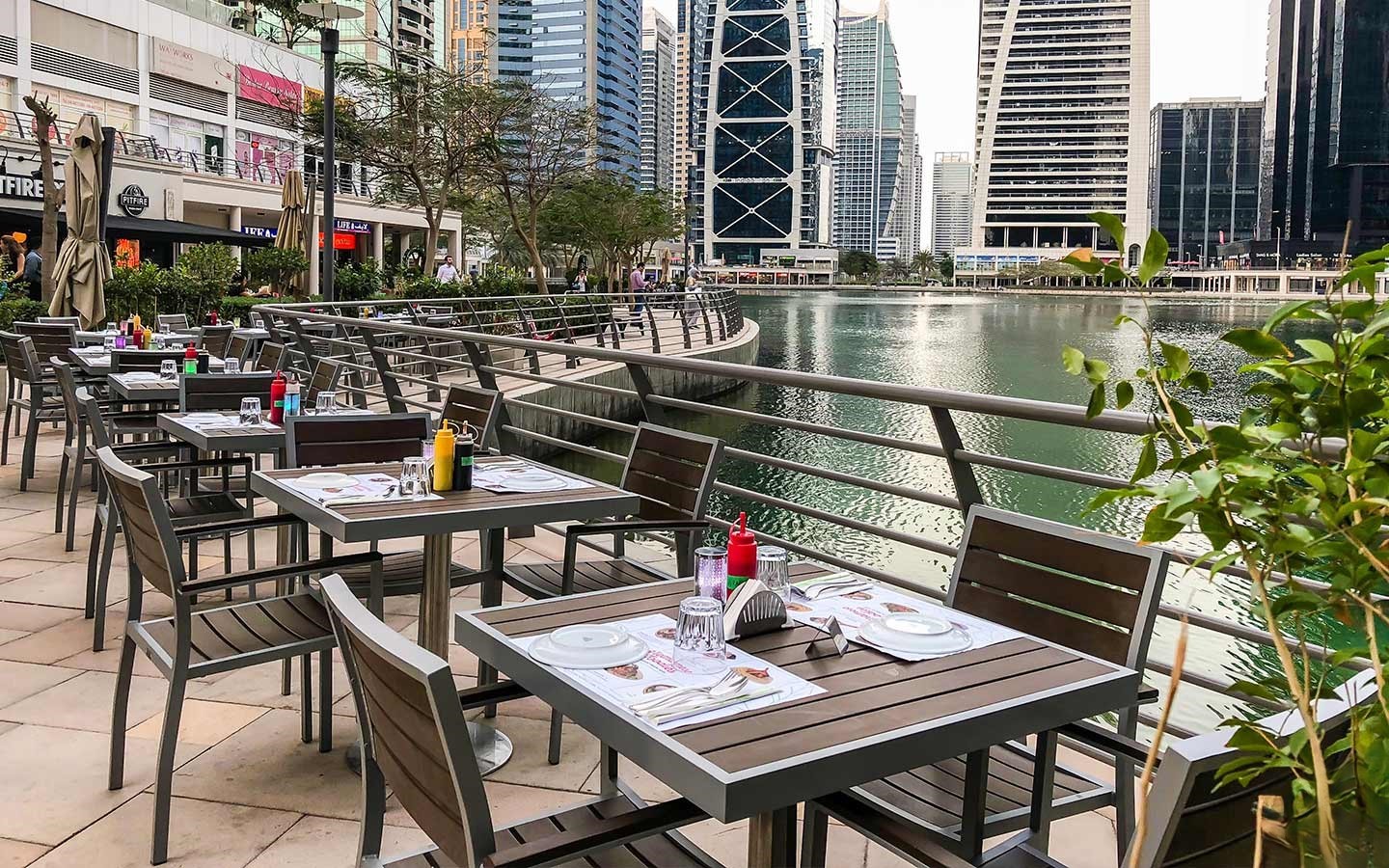Waterfront dining at Jumeirah Lake Towers with modern skyline, promenade seating, and scenic urban canal views.