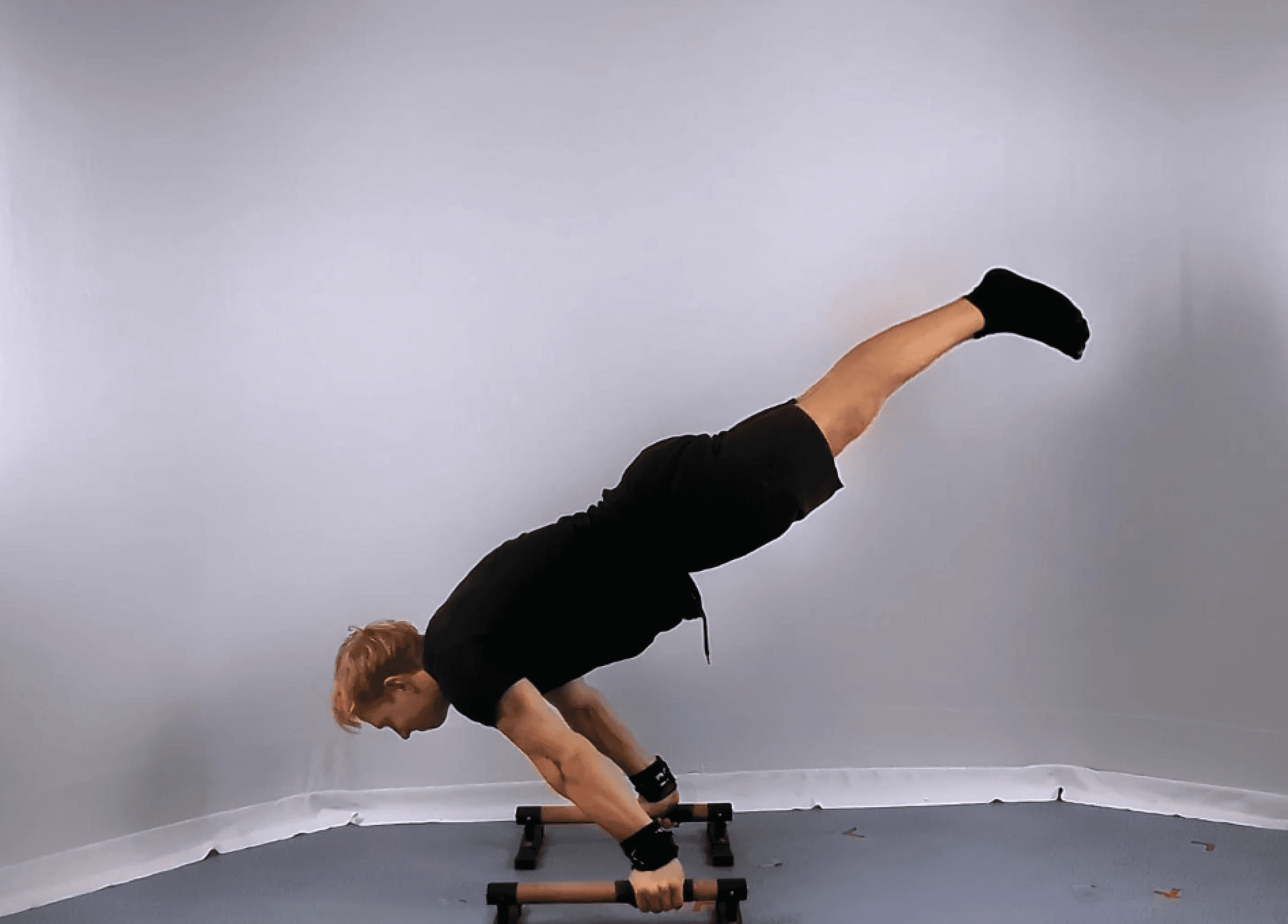 A person demonstrates impressive strength and balance while transitioning from a full planche to a handstand with momentum on parallel bars, in a minimalist indoor setting.