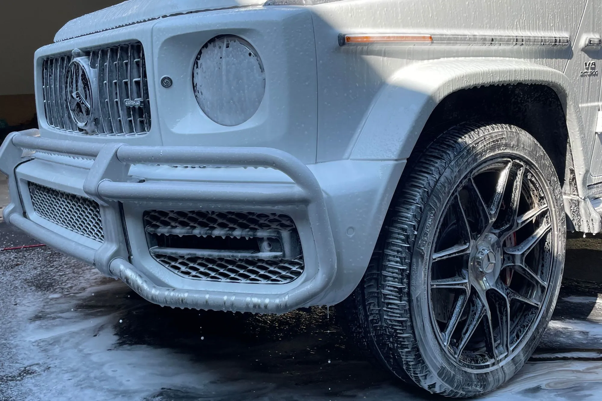 Detailer hand-washing a black vehicle with soap and a sponge