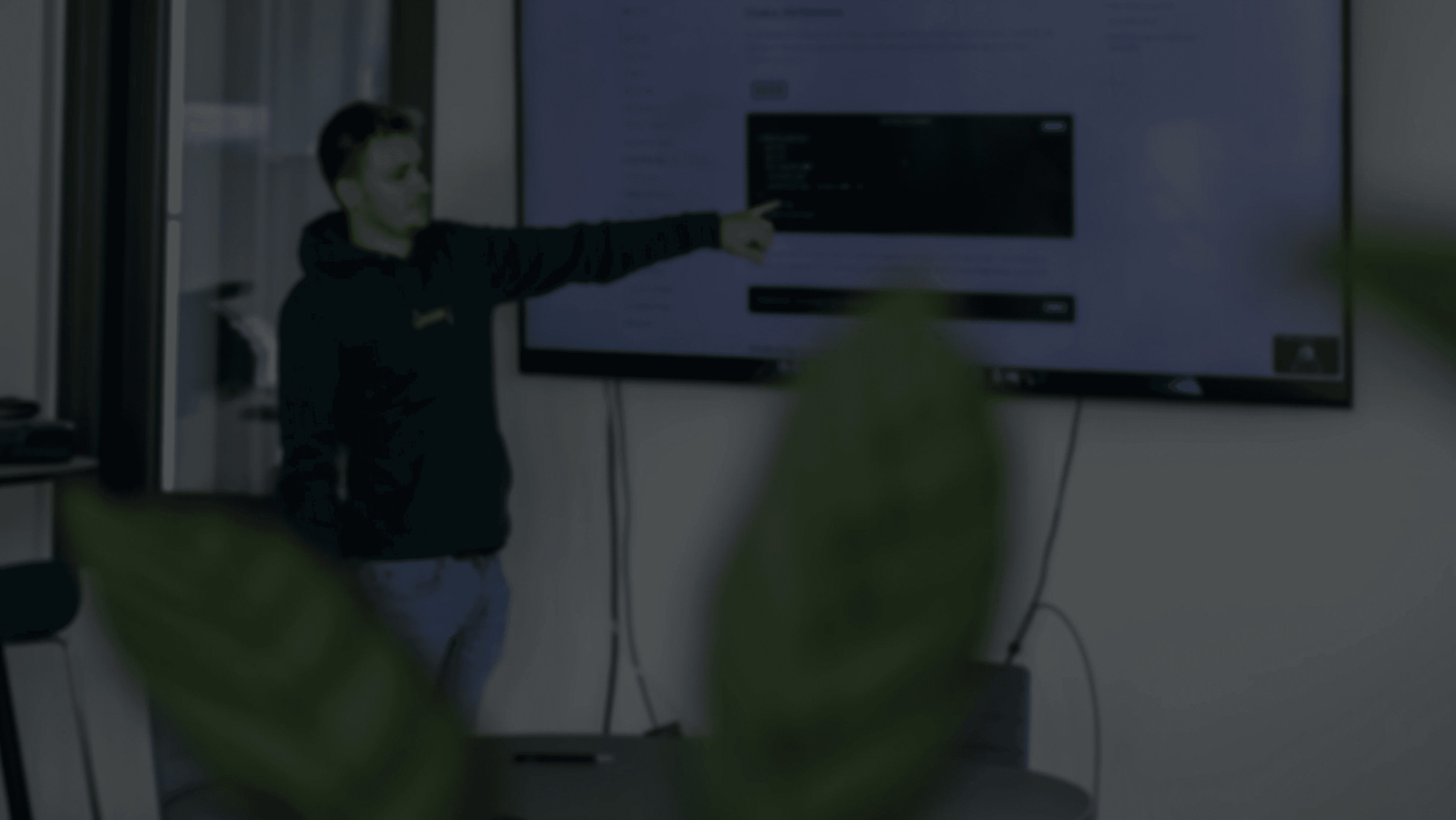 Eine Person steht vor einem Fernseh und zeigt auf einen Codesnippet und erklärt dabei etwas