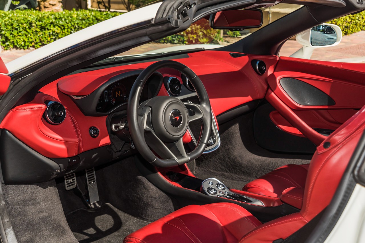 Close-up of the McLaren 570S cockpit, highlighting the leather-wrapped steering wheel, digital driver display, and sporty red interior.