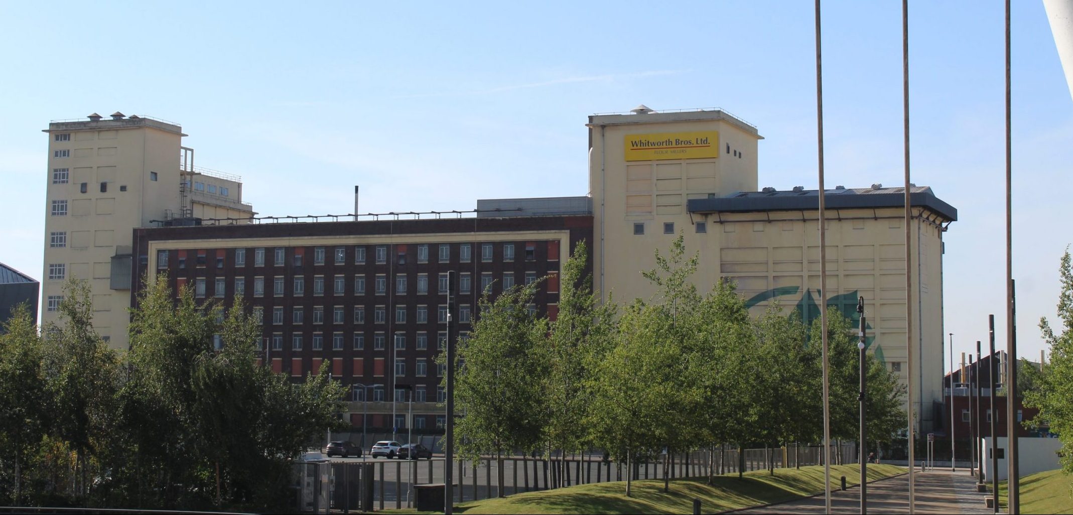 A modern building with multiple levels, featuring large windows and landscaping at the front under a clear sky.