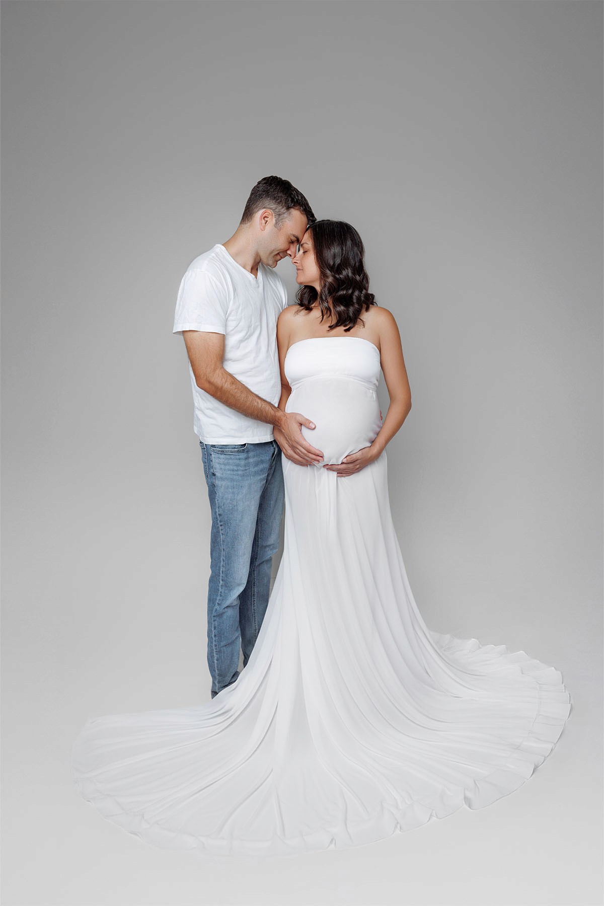 Maternity couple photoshoot — expecting parents sharing a warm, emotional moment together in studio.