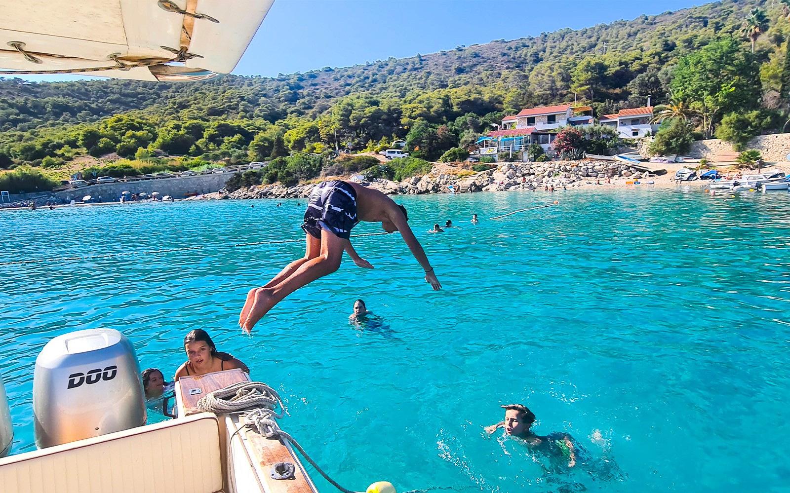 一個人在克羅地亞的維斯附近，跳入清澈的藍水中，旁邊有游泳者。