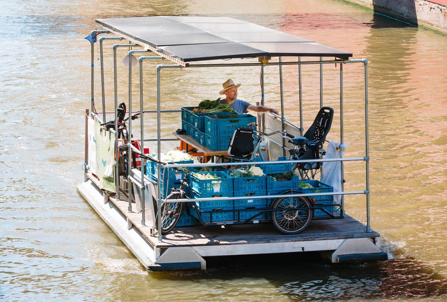 Smiling young woman with long hair standing against a dark green background, holding a finger to her chin.