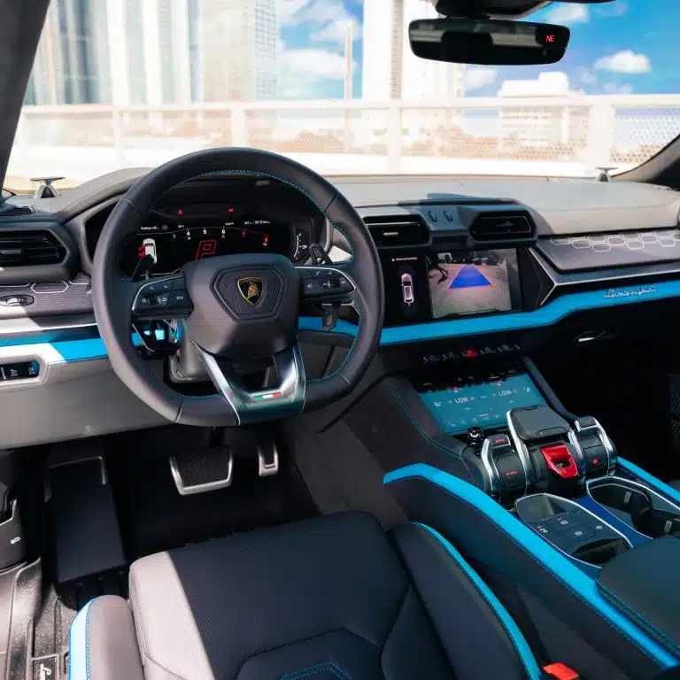 Driver's cockpit view of the Lamborghini Urus SE interior, featuring the steering wheel, digital displays, and vibrant blue accents.