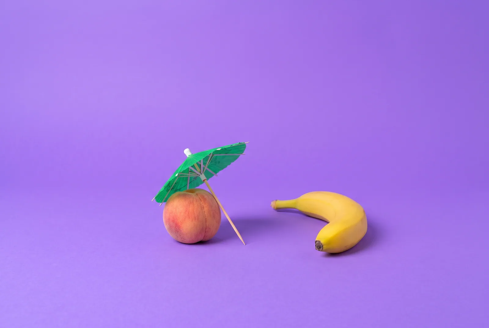 A tiny umbrella sheltering a peach while a banana stands outside it, a playful QUITTR vs Canopy comparison