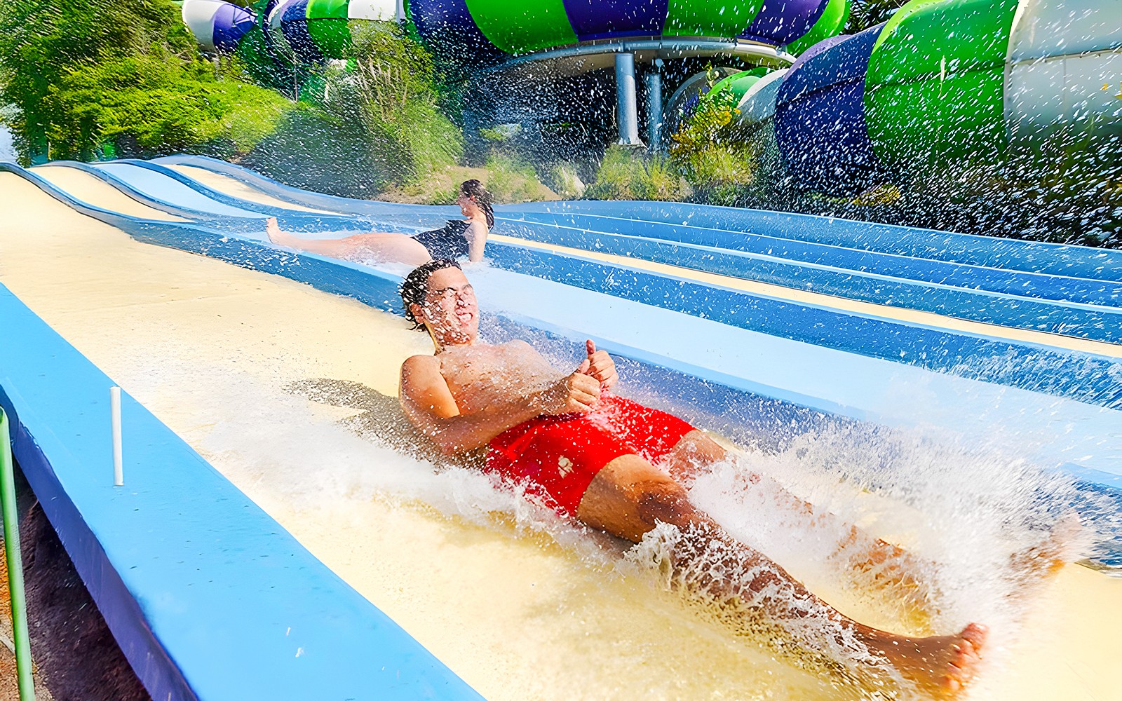 People sliding down Pistas Blandas water slide at Aquopolis, splashing water.