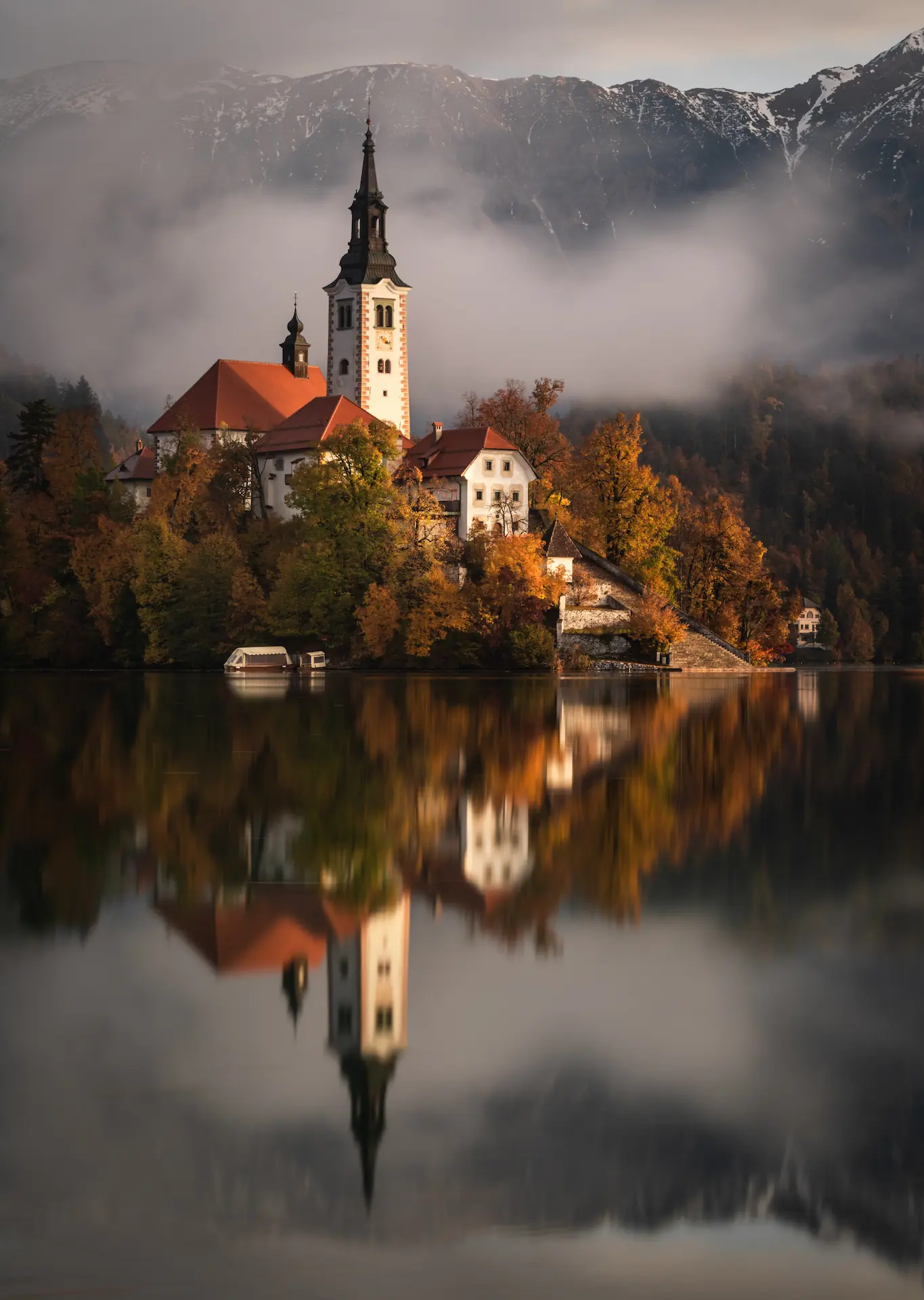 A serene landscape of Lake Bled, Slovenia, featuring a church on the Bled Island reflected in calm waters, surrounded by mist and trees.