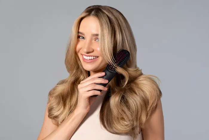 A woman smiling as she brushes long blonde hair with a styling brush