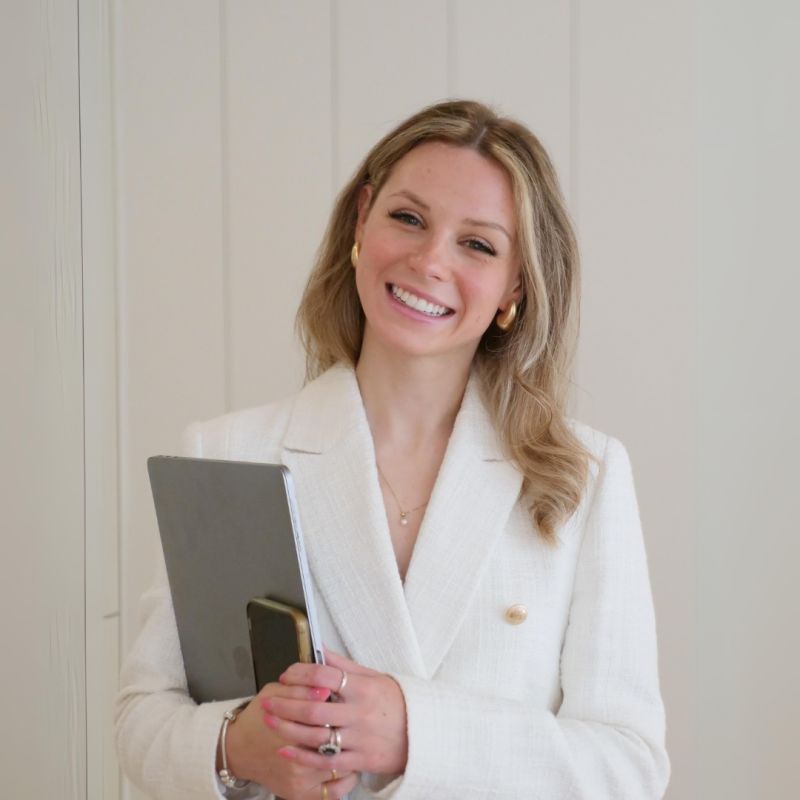 A woman with auburn hair and a gray coat over a white sweater, set against a neutral background, exuding a minimalist aesthetic.