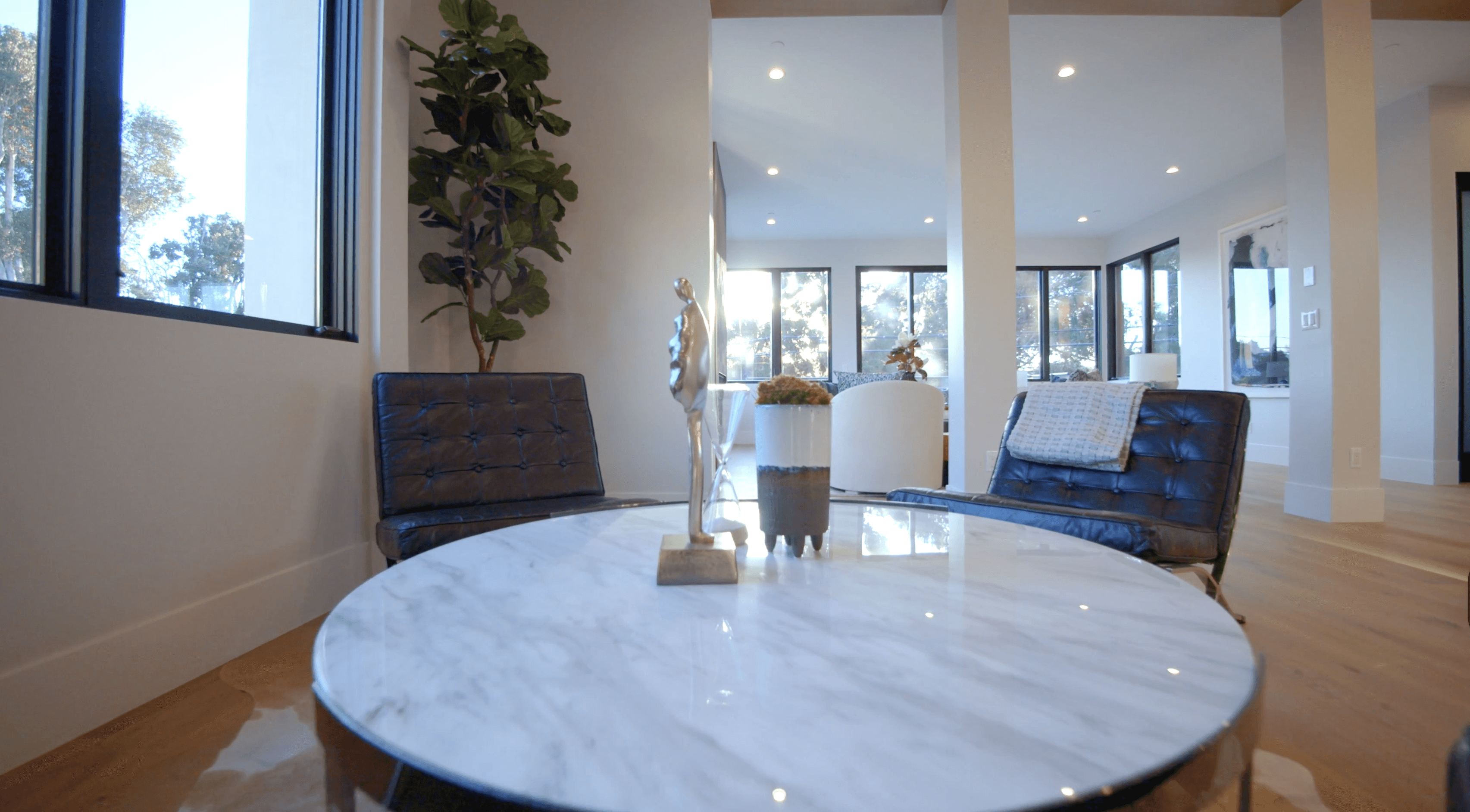 A cozy interior space featuring a marble-topped table and two chairs, with bright windows in the background.