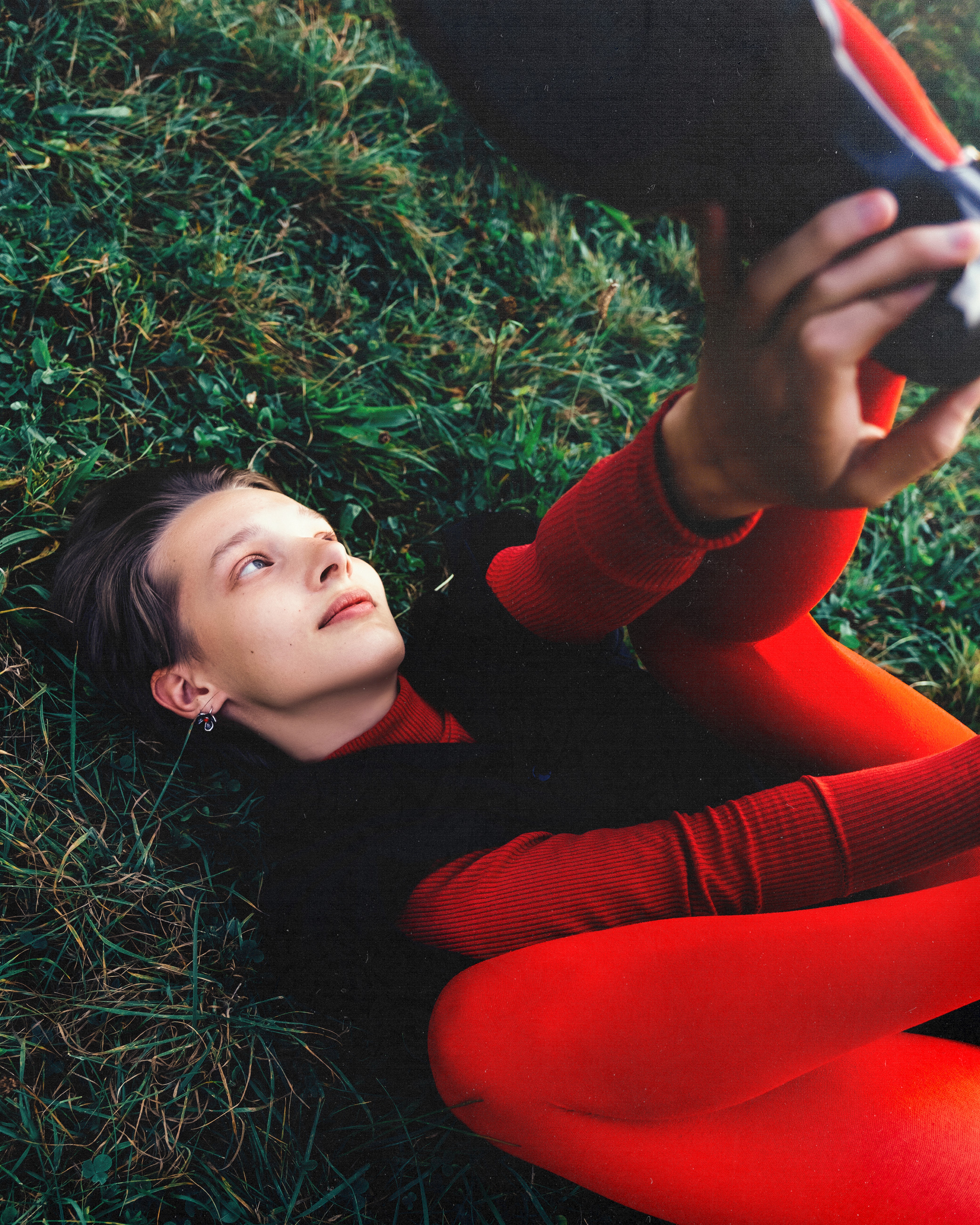 Ewa – Red Persona - lying in the grass, lifting her foot.