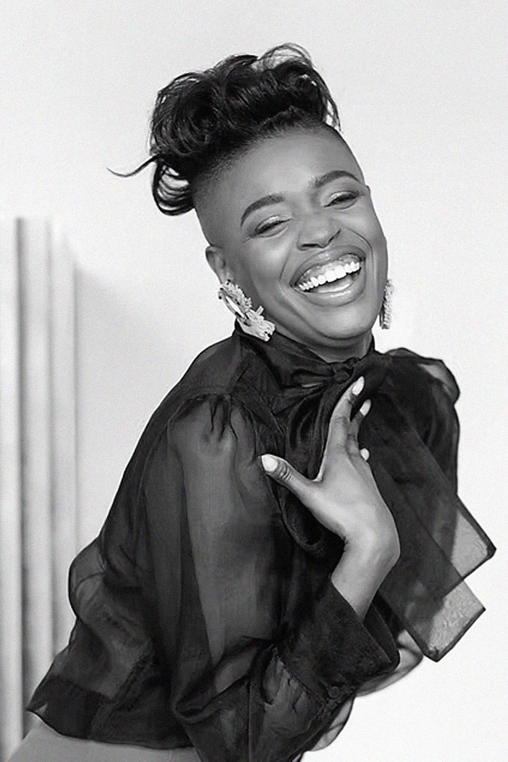 Smiling young man with curly hair, wearing a dark hoodie, against a softly lit background.