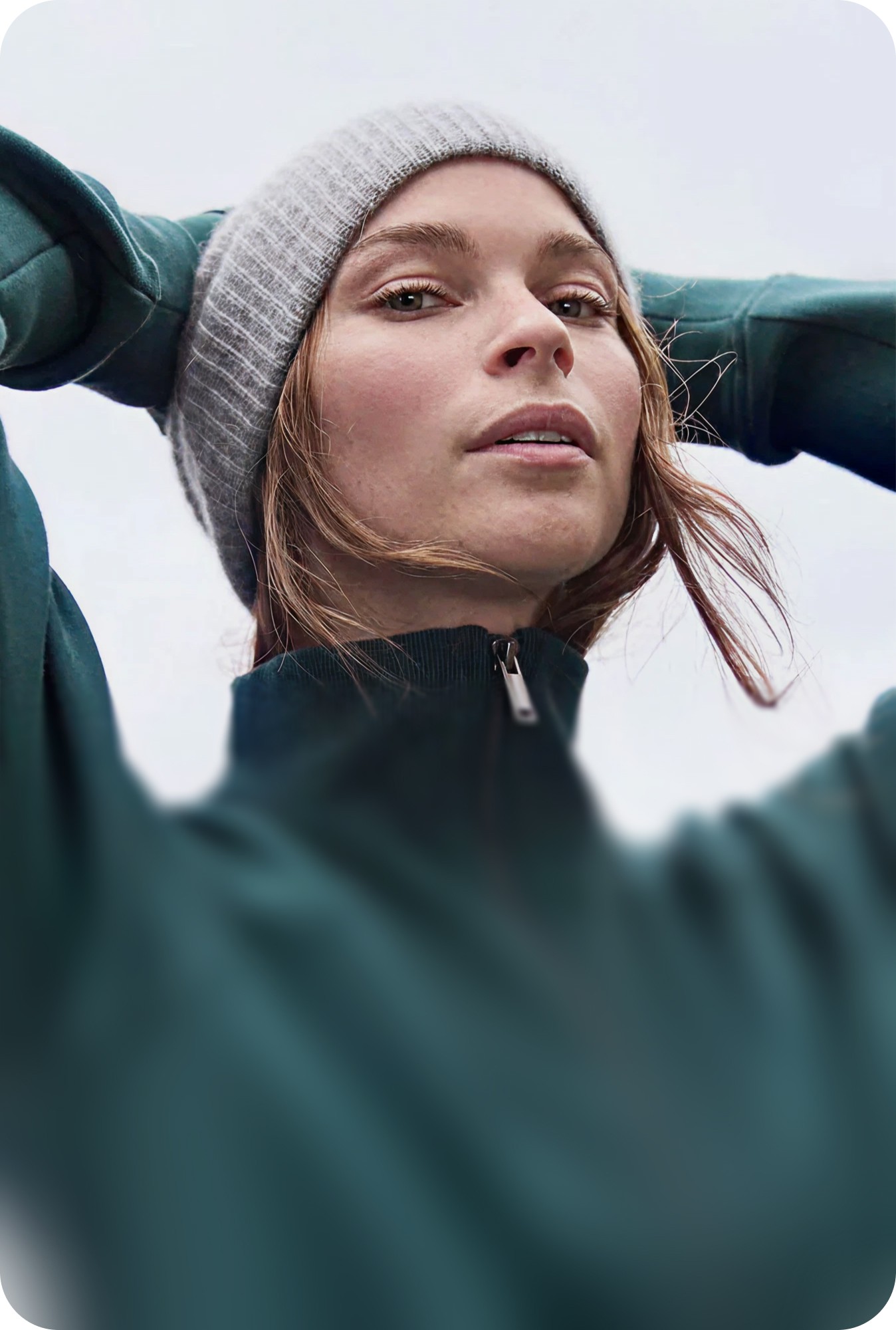 A woman wearing a beanie and athletic clothing looking upward while exercising outdoors.