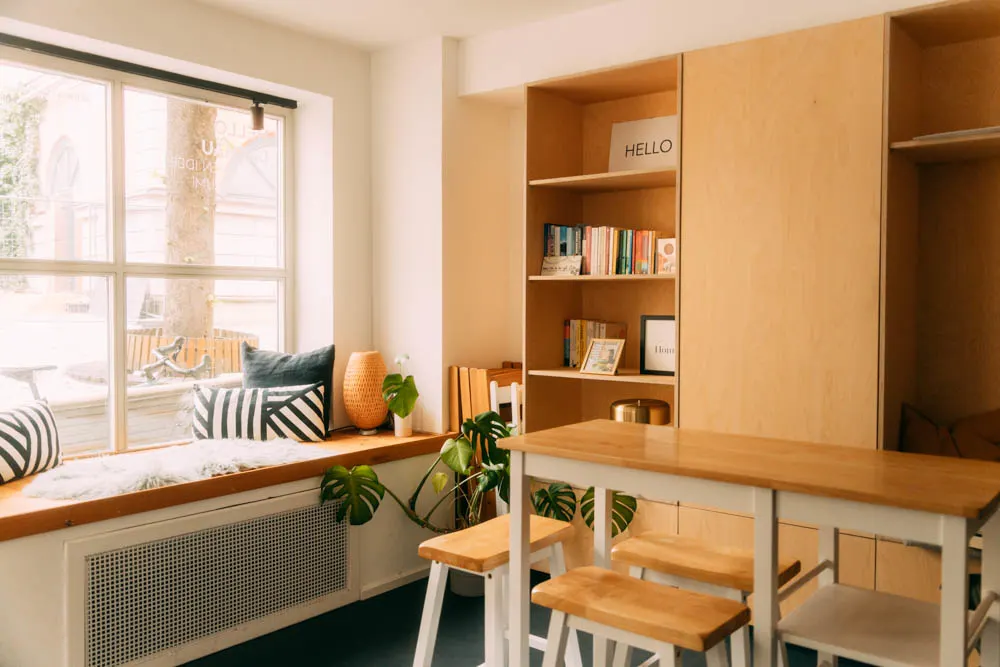 Gemütliche Leseecke mit Holztisch, Bücherregal, Monstera-Pflanze und Kissenbank in modernem Coworking-Space in Dachau.