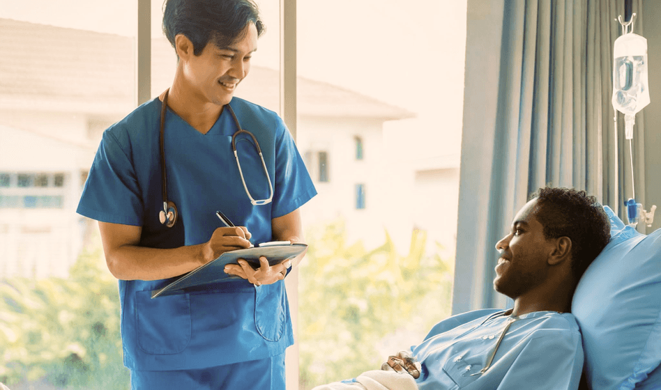 Medical personnel holding a clipboard, smiling at a patient in a hospital bed with trees visible outside.