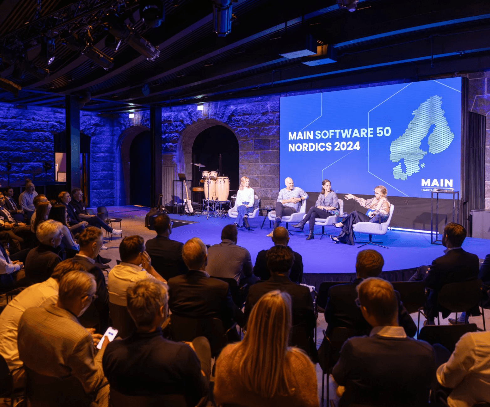 Eine Gruppe von Menschen auf einer Konferenz, bei der vier Menschen auf der Bühne stehen.