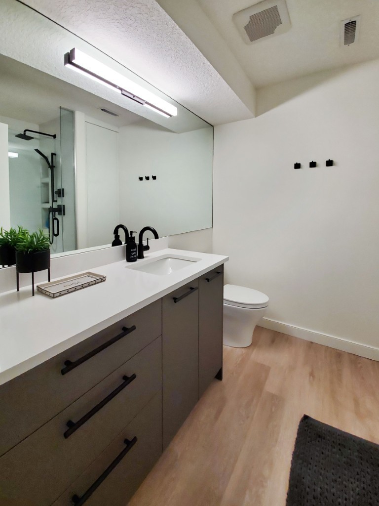 Image of Modern primary ensuite bathroom with sleek gray cabinets, white countertop, and black fixtures by KHD Homes.
