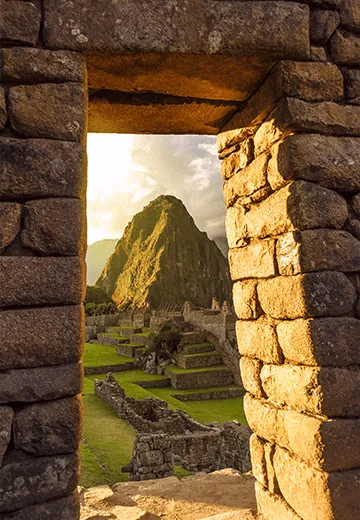 Vista de Machu Picchu através de portal de pedra inca, com terraços e montanhas ao fundo no Peru