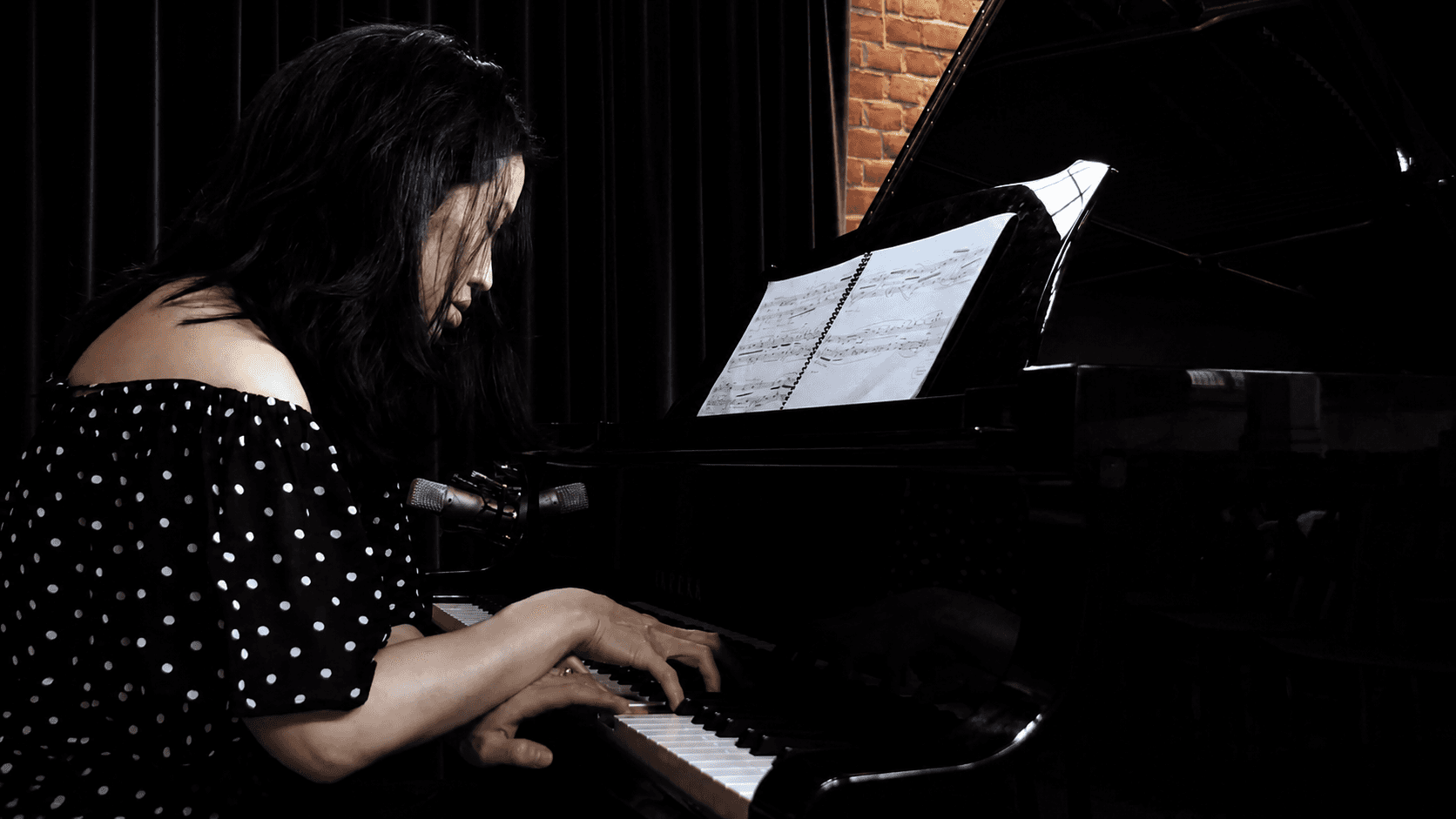 Pianist performing at a grand piano with an open score on the music stand.