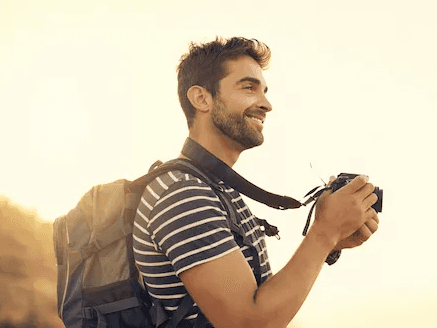 Viajante com mochila e câmera apreciando paisagem ao pôr do sol