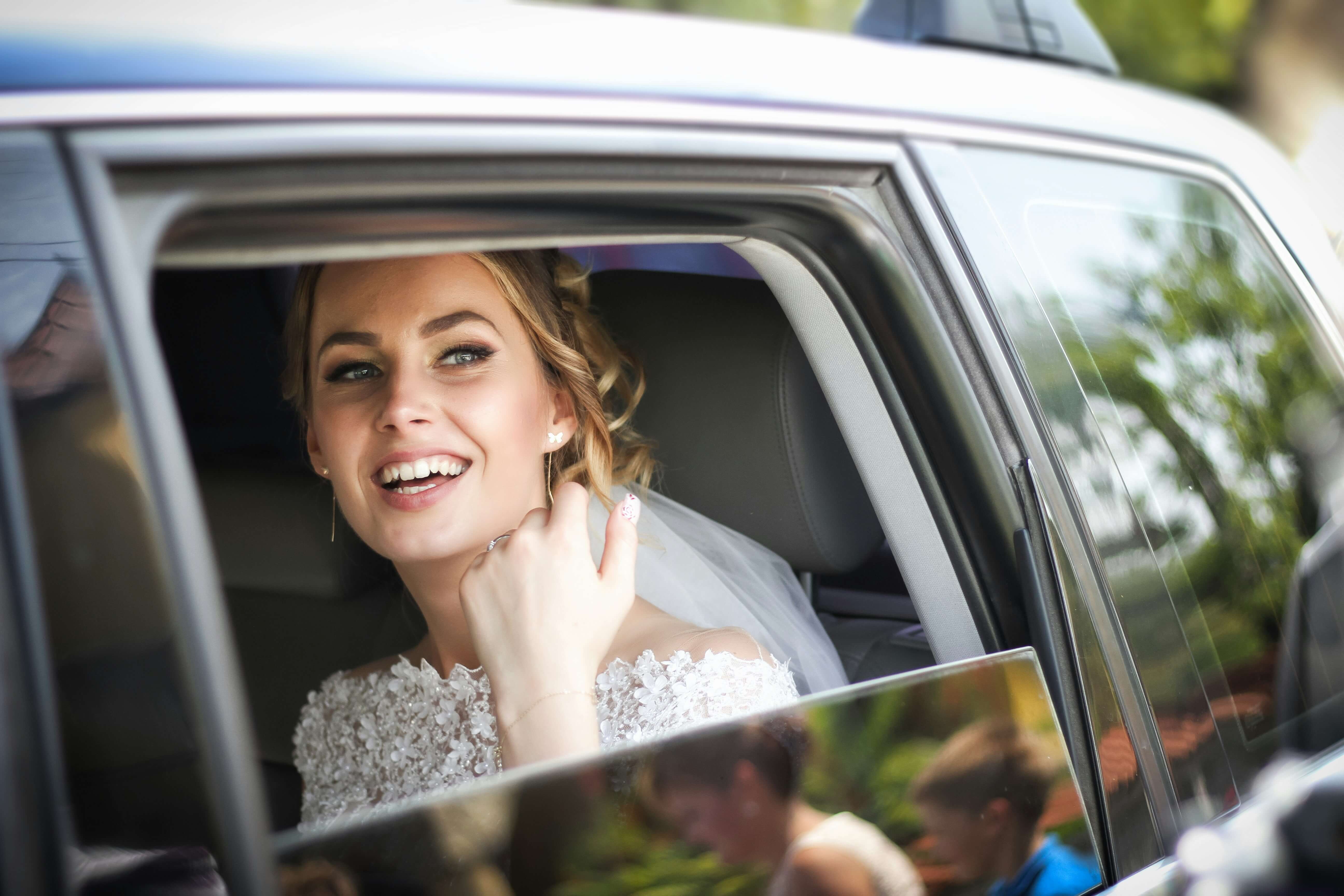 Smiling bride with elegant makeup looking out of a car window, showcasing bridal makeup done by Sam Hoult Beauty in Hull.