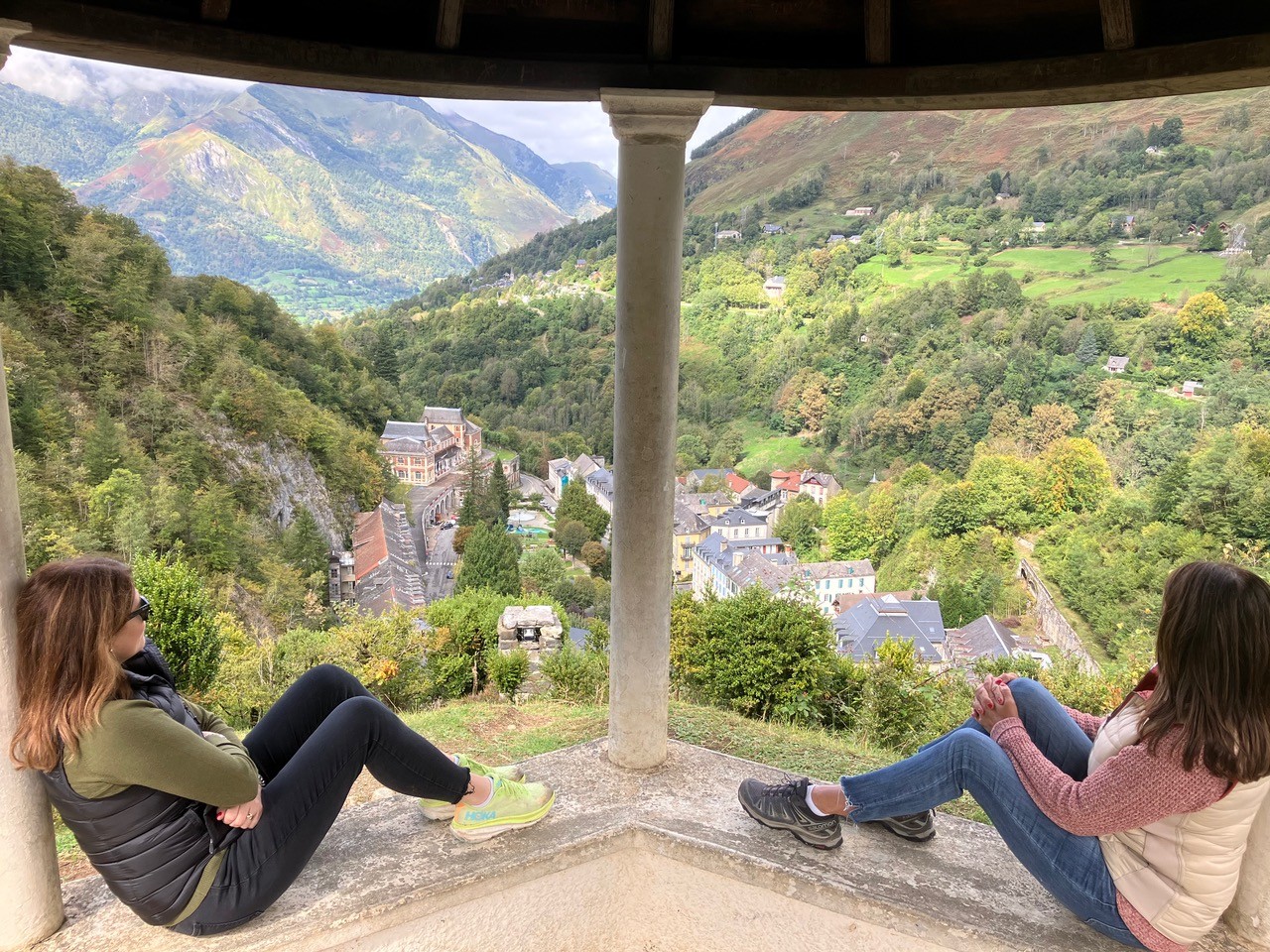 Guests admiring a panoramic view over a historical village tucked in the Ossau Valley from a mountain gazebo, representing the heritage discovery tours offered by The Basque Way.