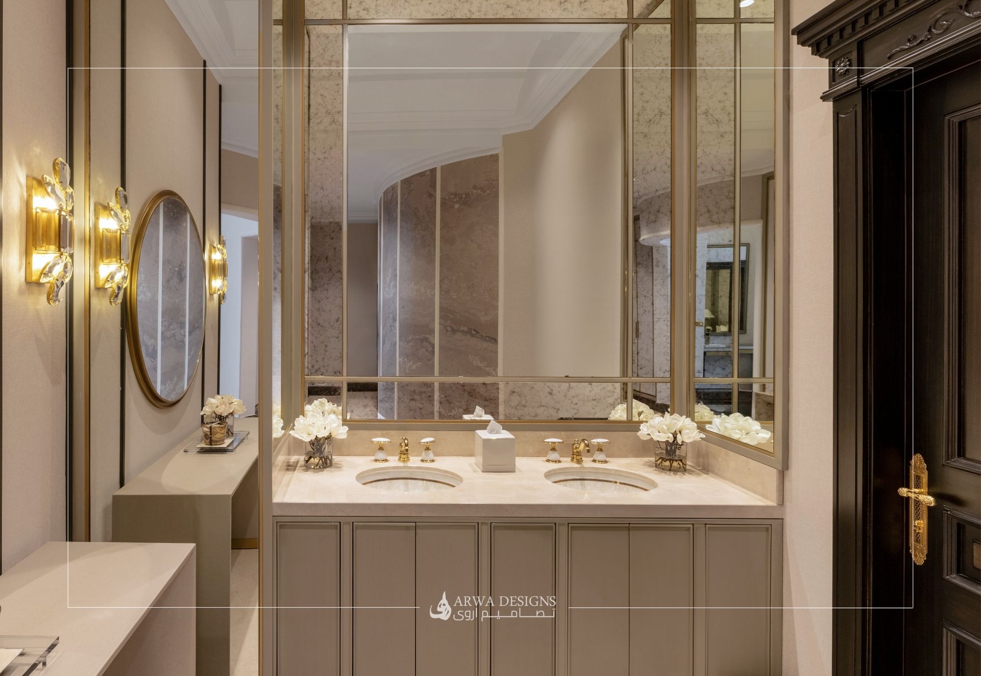 تصميم حمام ضيوف نيو كلاسيك يحتوي على مغاسل مزدوجة، خزائن بلون توب دافئ، إضاءات كريستال، ومرايا تمتد للسقف.