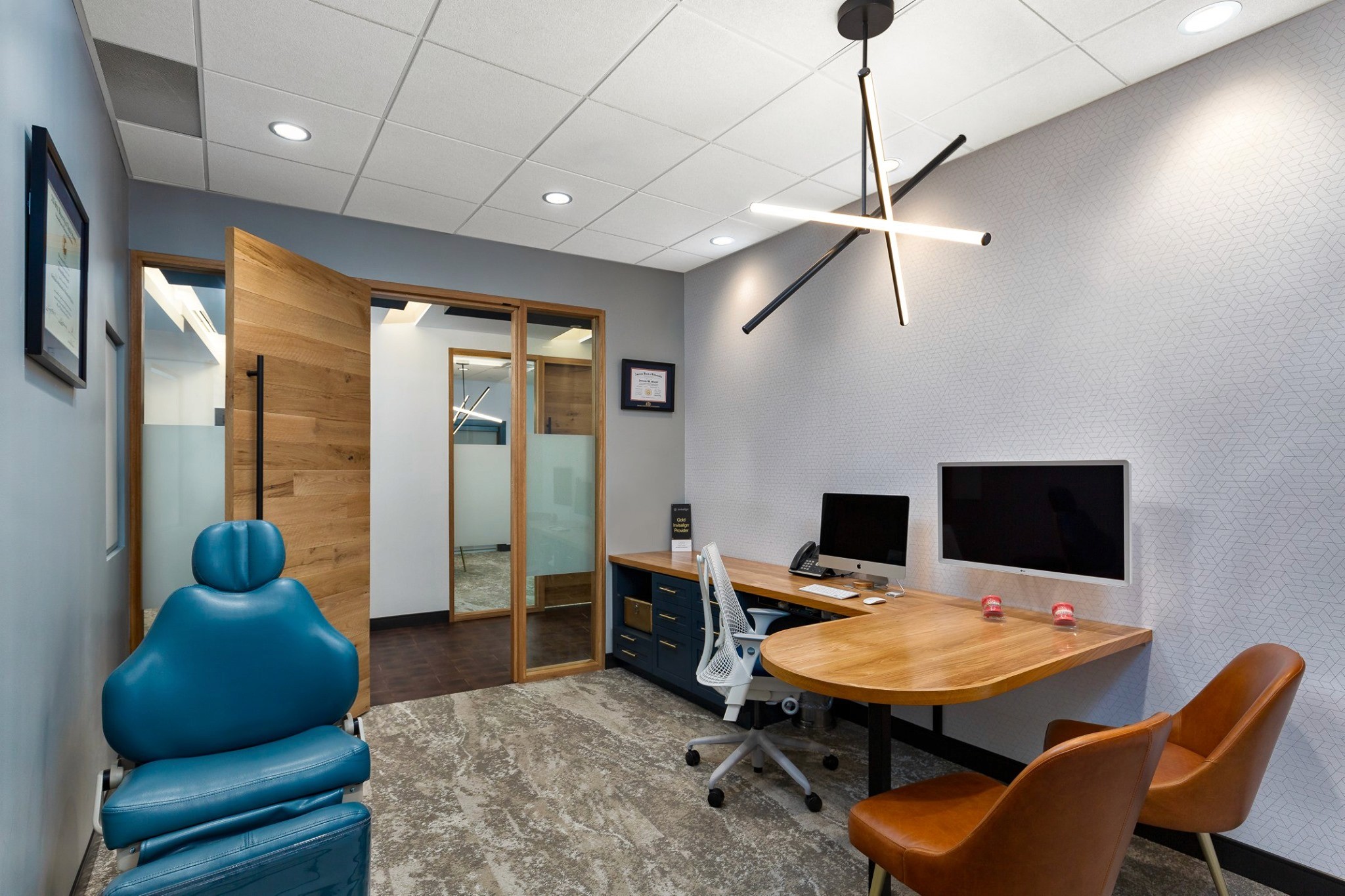 A modern office space with a wooden desk, two computers, a chair, and a blue decorative item in the corner.