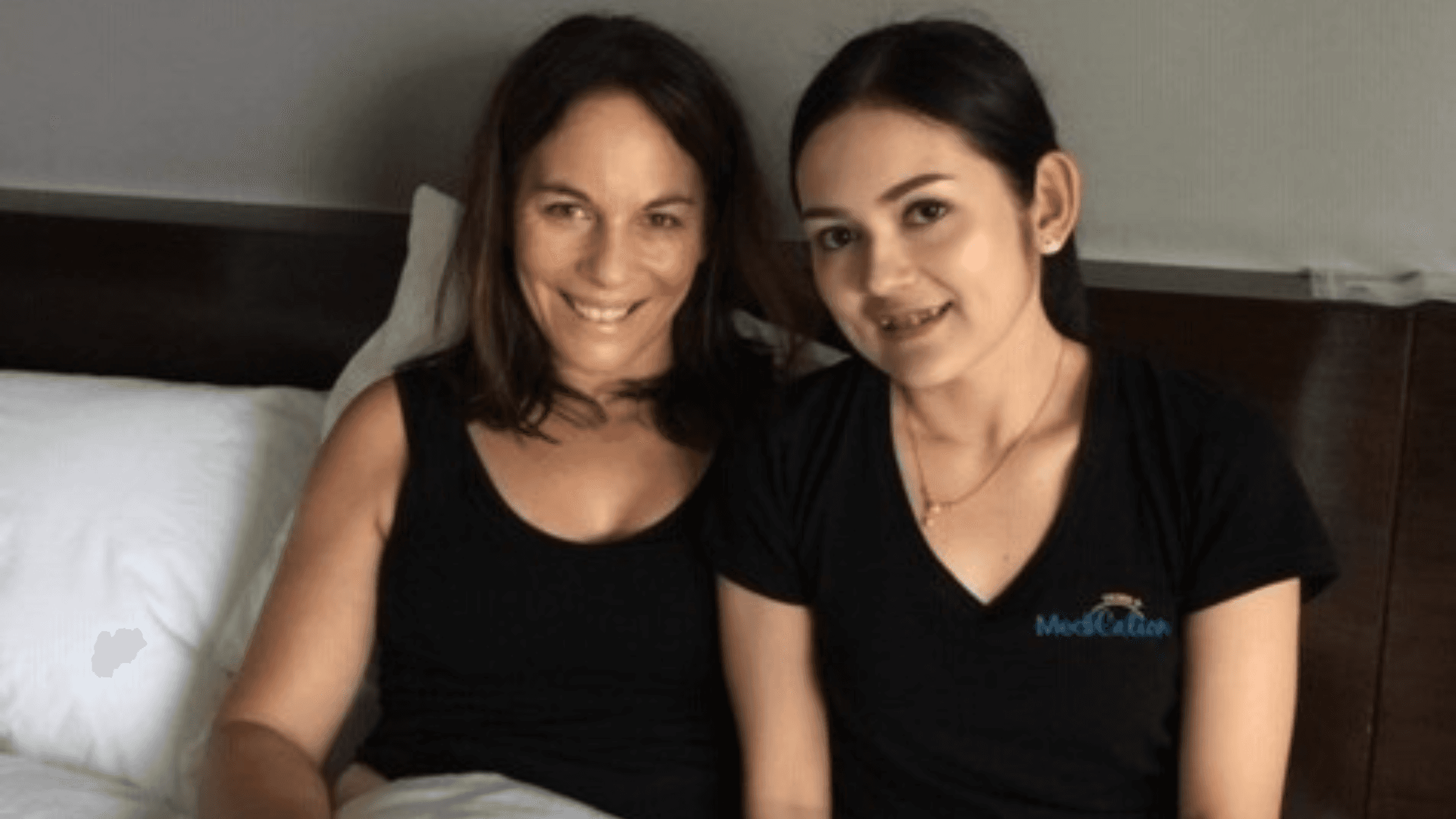 Two women smiling together indoors, one wearing a black MediCation Tours t-shirt, sitting on a bed after a procedure.