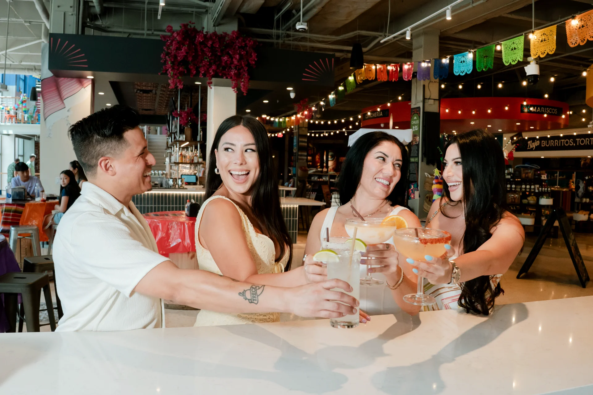 Friends toasting cocktails at the bar inside Mexico Ceaty, with the Mariscos and Baja burrito stalls in the background