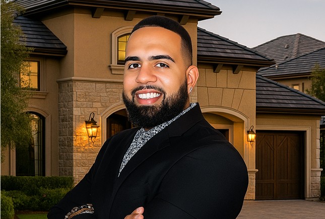 A portrait image of Jossue Guzman in a suit, posing in front of a Luxury Individual sub-urban house