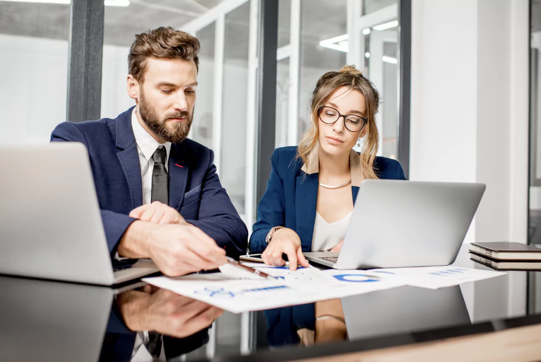 male and female colleagues sitting next to each other in front of computers in their office