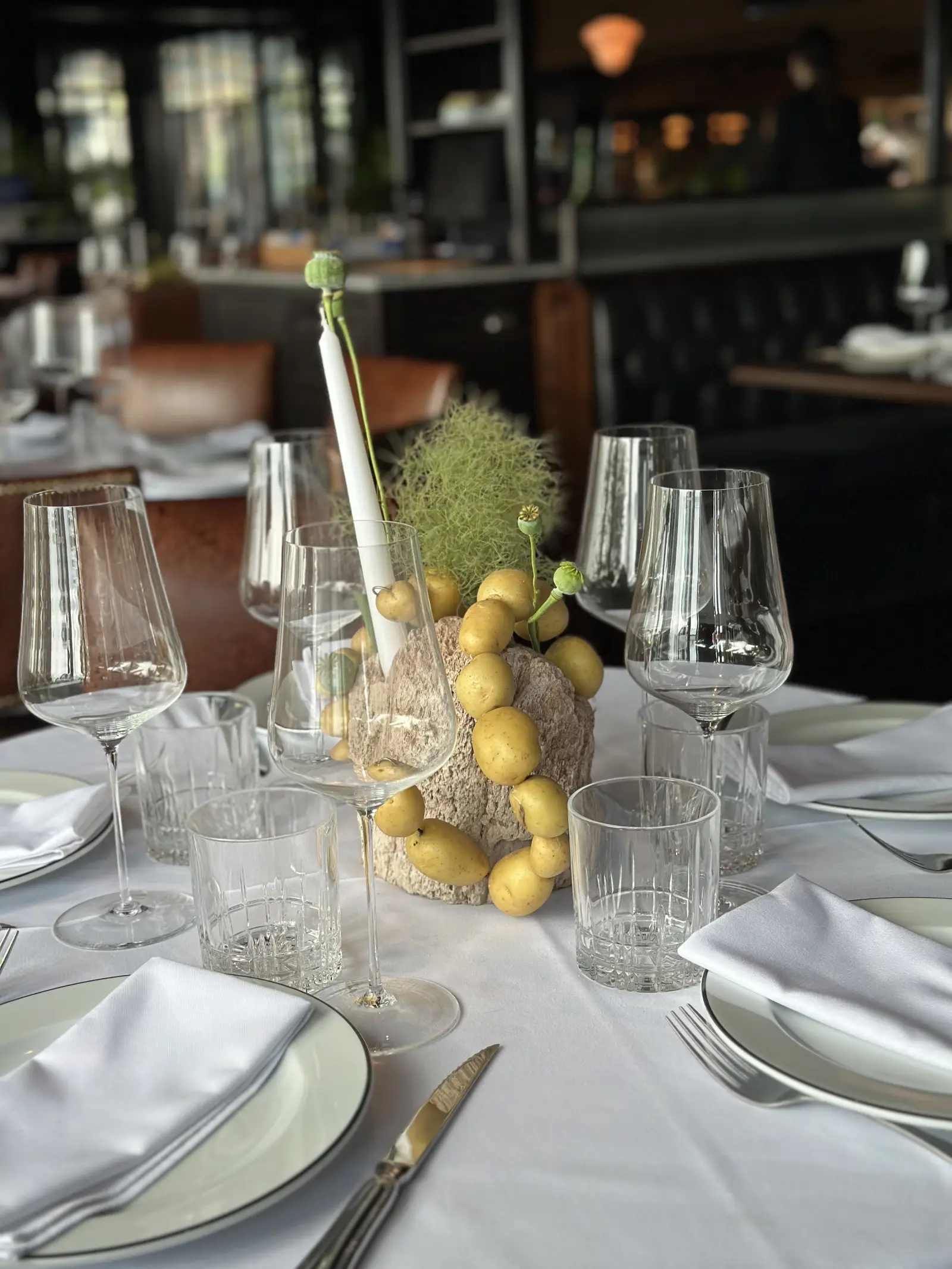 Centro de mesa conceptual con papines andinos ensartados, vela blanca y smoke bush verde en base de piedra gris.