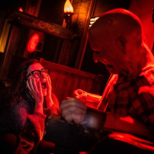 一位戴眼镜的惊恐女士在一个幽暗、红光弥漫的房间中面对一个凶险的光头人物时尖叫。