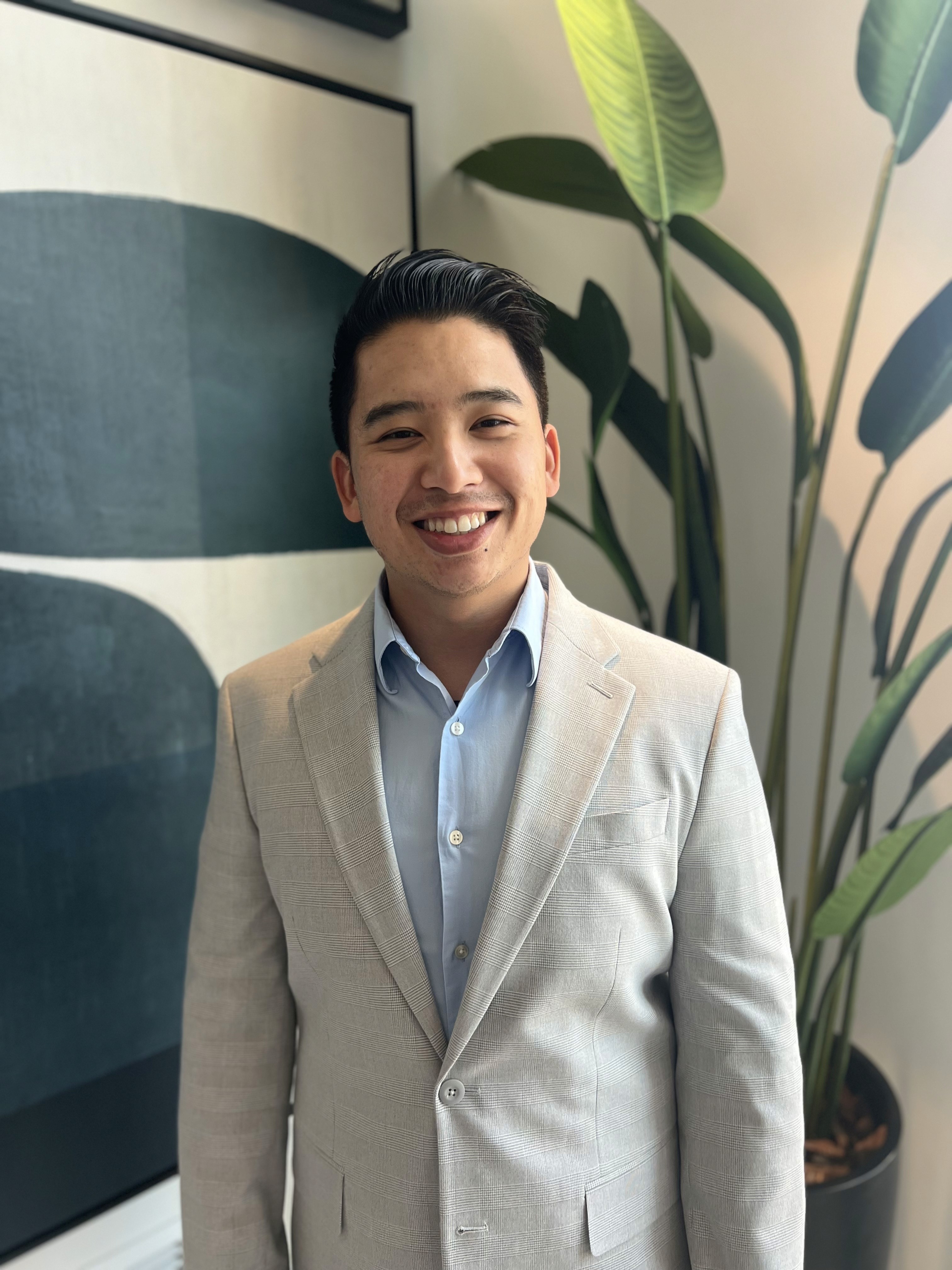 Young man with glasses in a gray hoodie, sitting in front of a computer screen with an orange background.