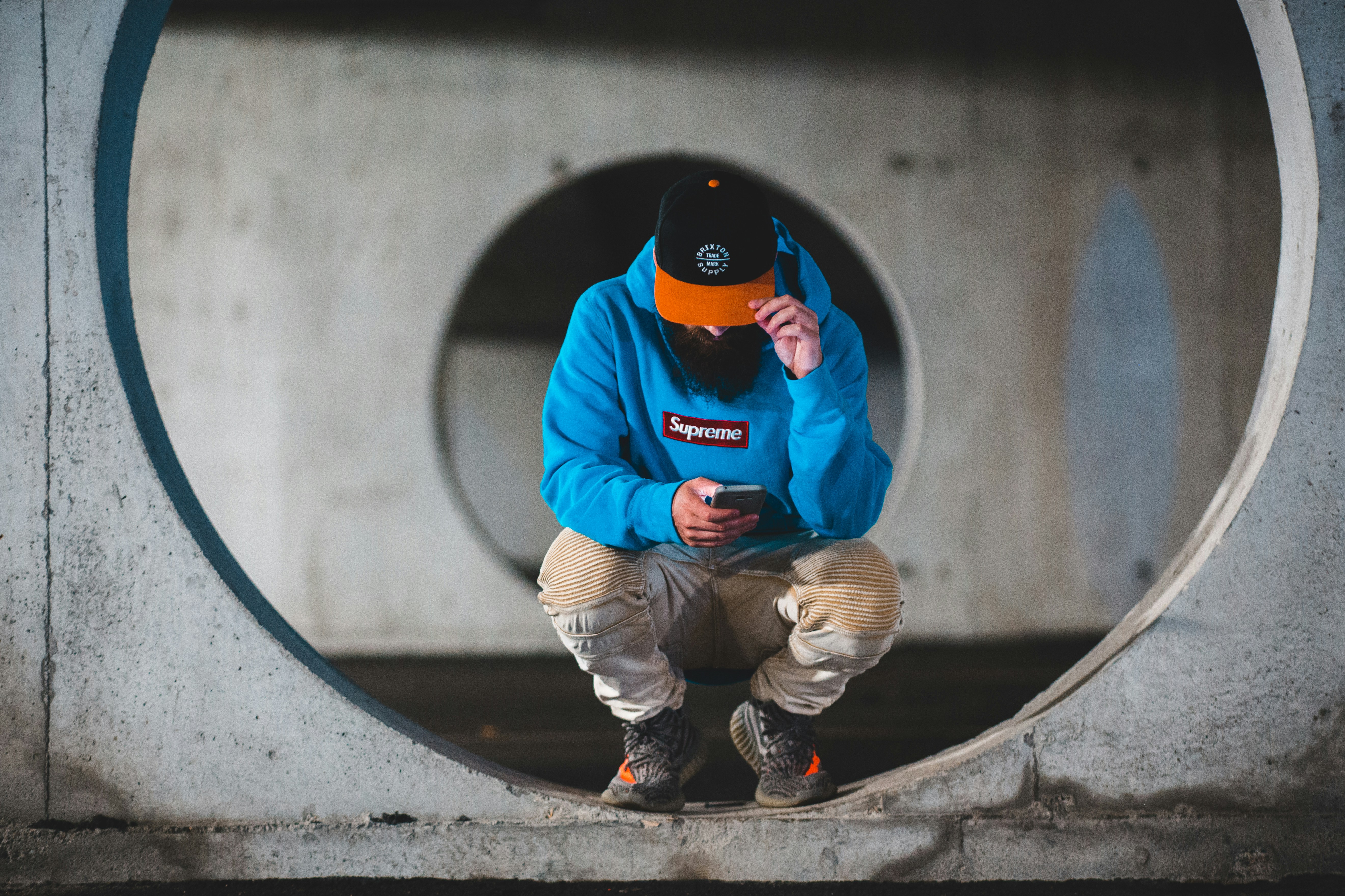 man in orange and black hoodie and gray pants sitting on concrete stairs