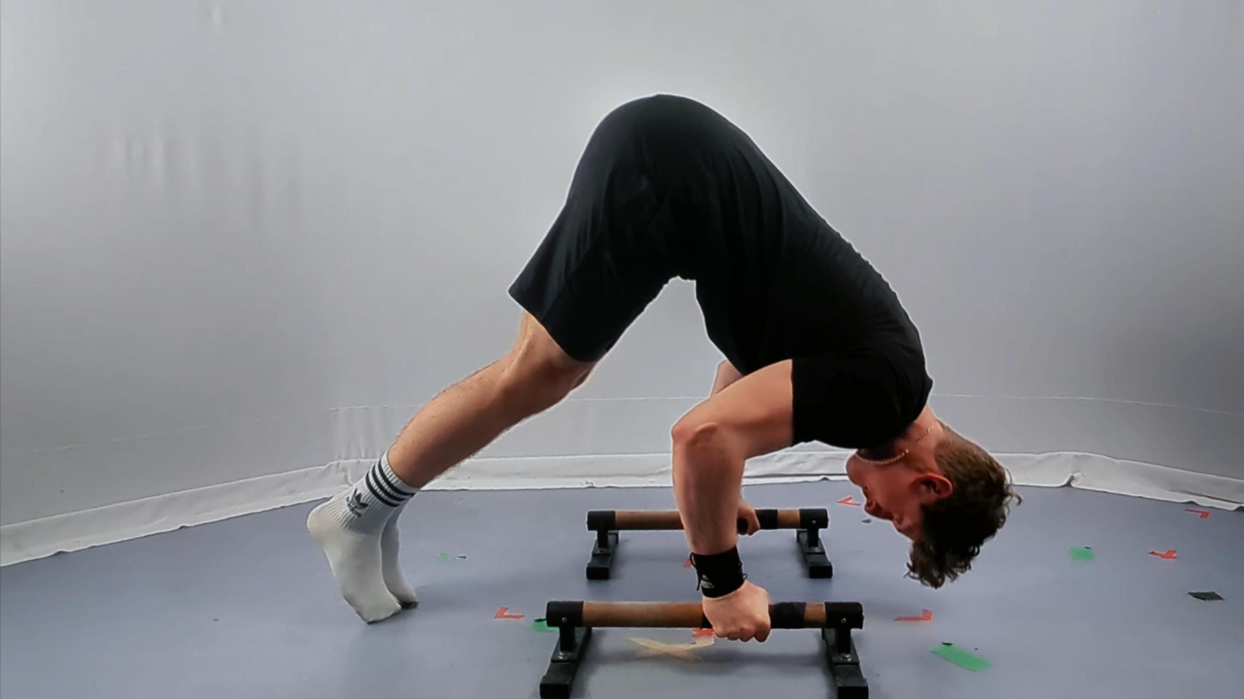 A man in athletic wear performs Calisthenics Pike Push Ups on handles in a minimalist room, demonstrating proper form and balance.