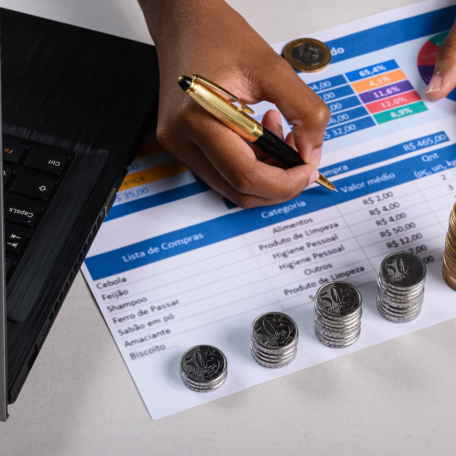 A person holds a pen while reviewing a detailed expense report on a desk, surrounded by stacks of coins, emphasizing financial planning and budget management.
