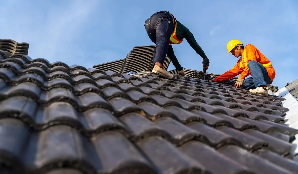 Two contractors performing summer roof maintenance on a residential tiled roof under a clear blue sky