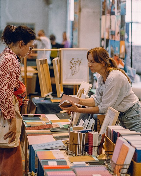 Zdjęcie przedstawiające wystawczynię podczas rzedaży swoich notesów i zeszytów.