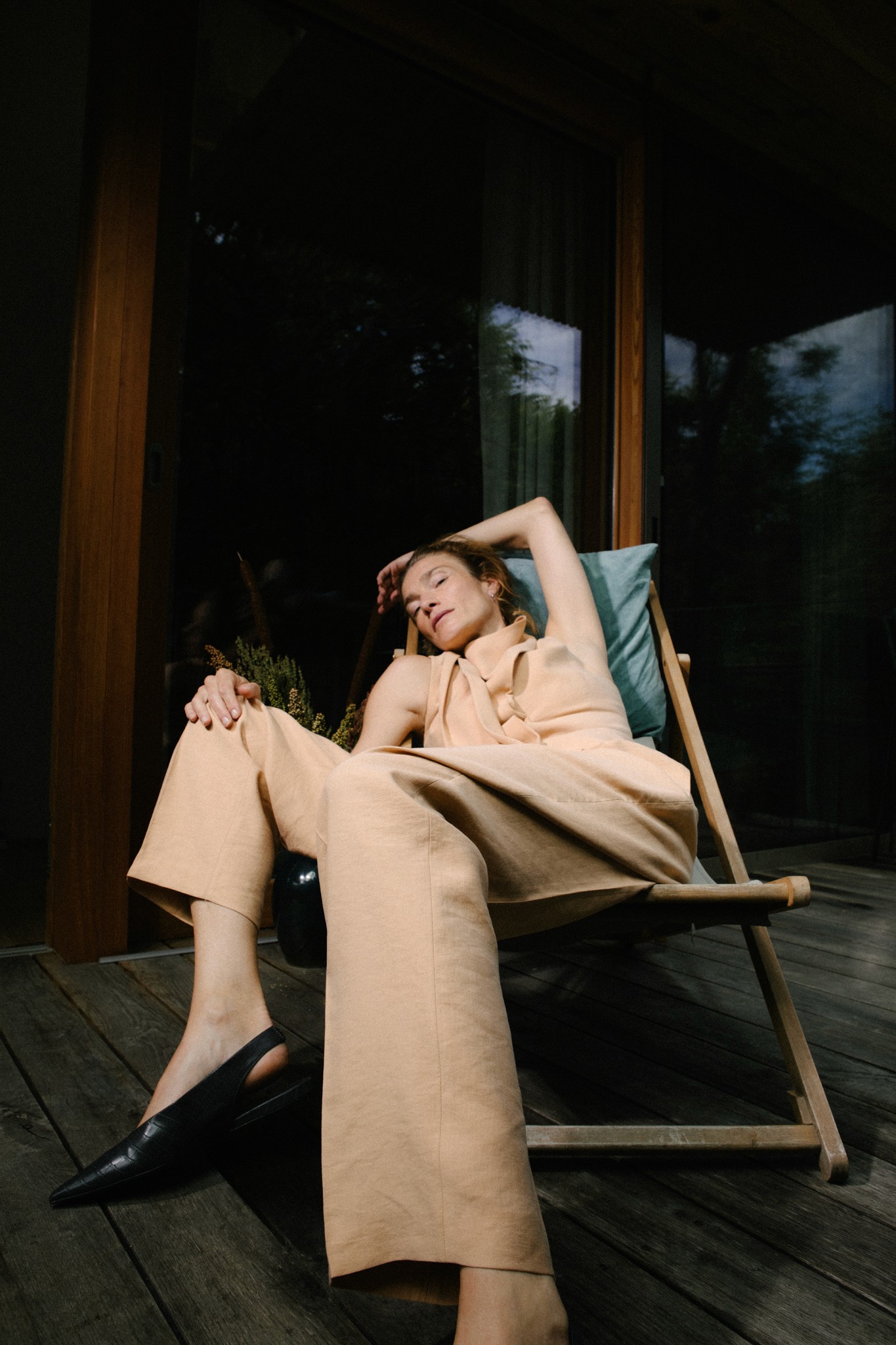 Frau entspannt im Liegestuhl auf Holzterrasse vor modernem Haus