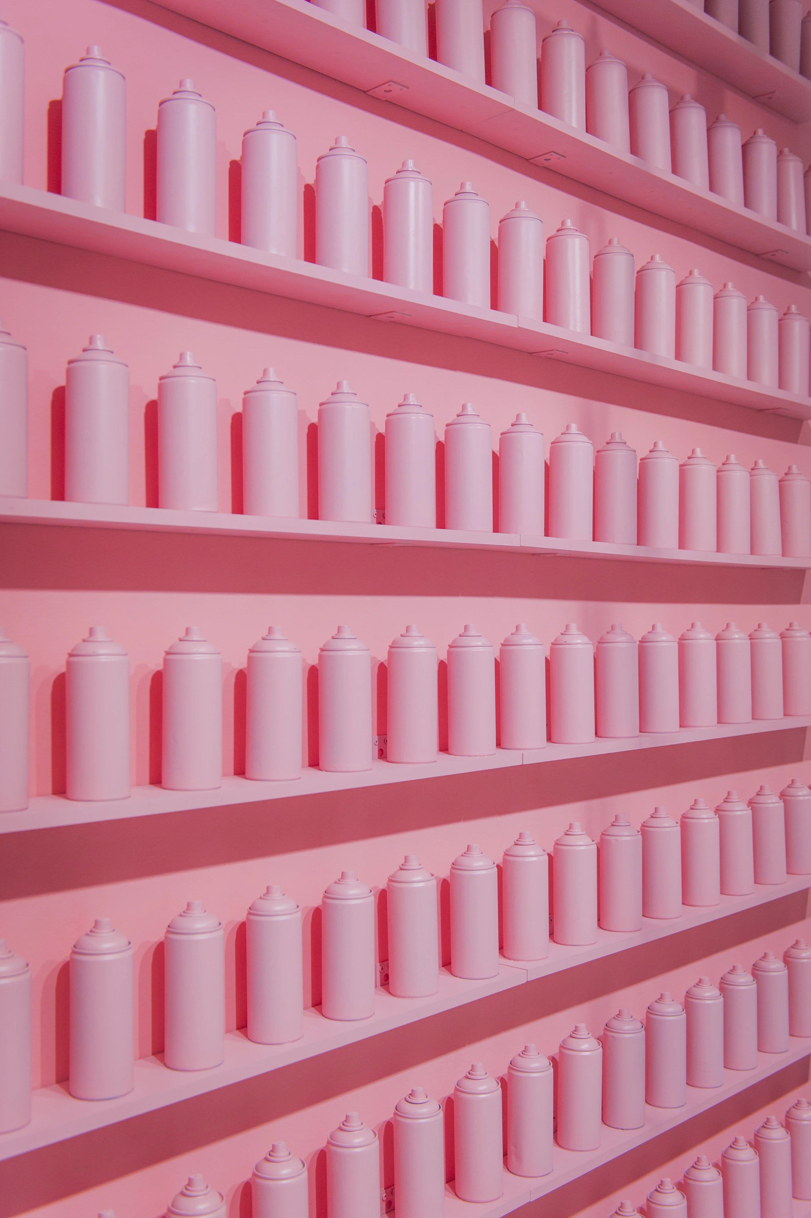 Monochrome pink installation wall at FREIRAUM SHOP with rows of identical pink spray cans on pink shelves.