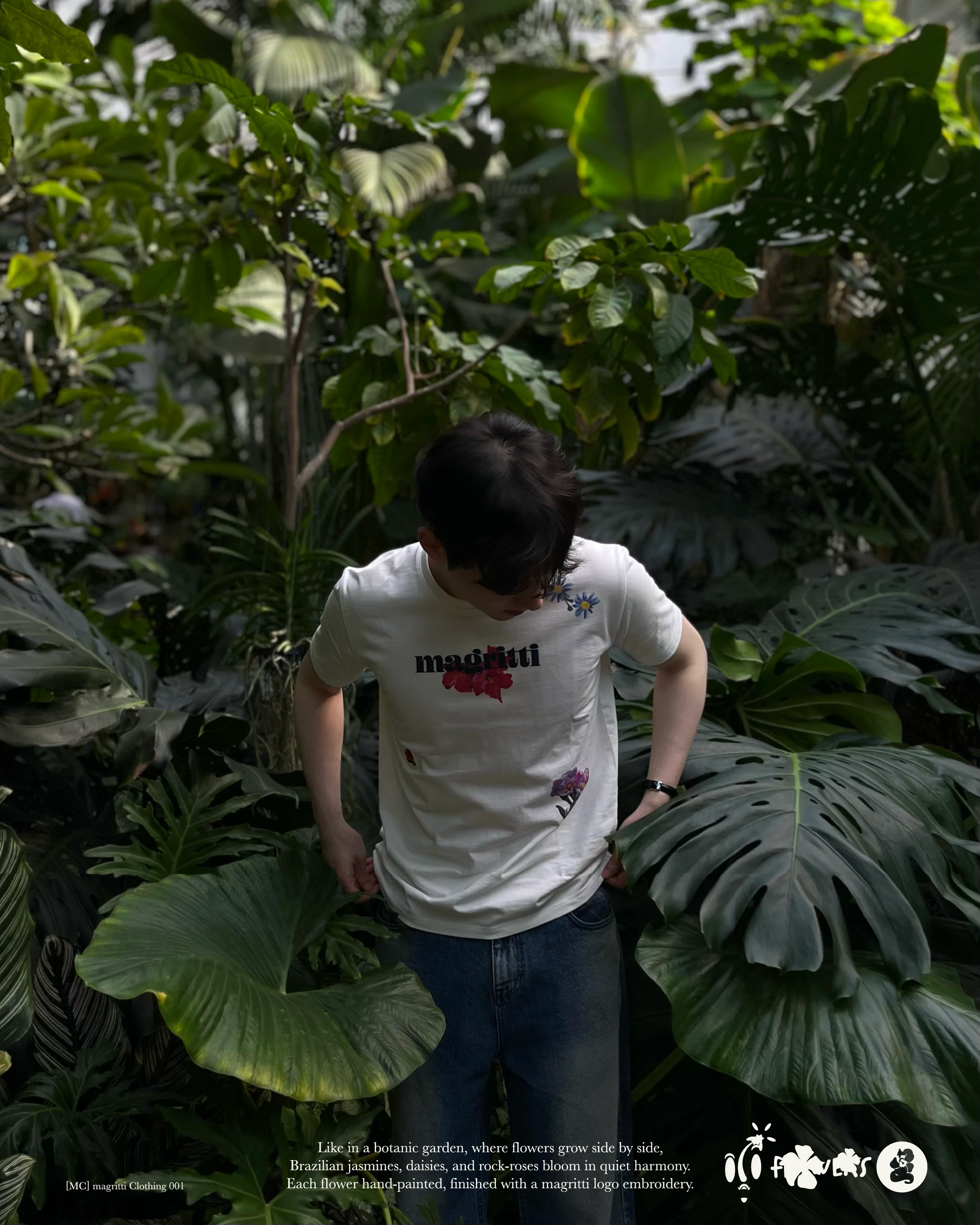 A person in the printed white shirt and jeans, standing among large green leaves, head lowered.