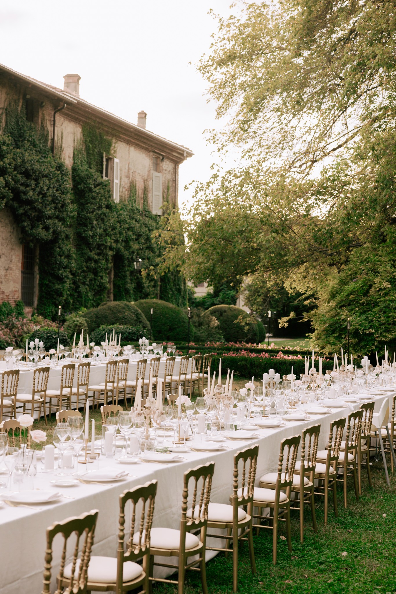 Ricevimento matrimoniale a Villa Ferrari con tavoli allestiti nel parco, sedie dorate e fiori bianchi sotto gli alberi