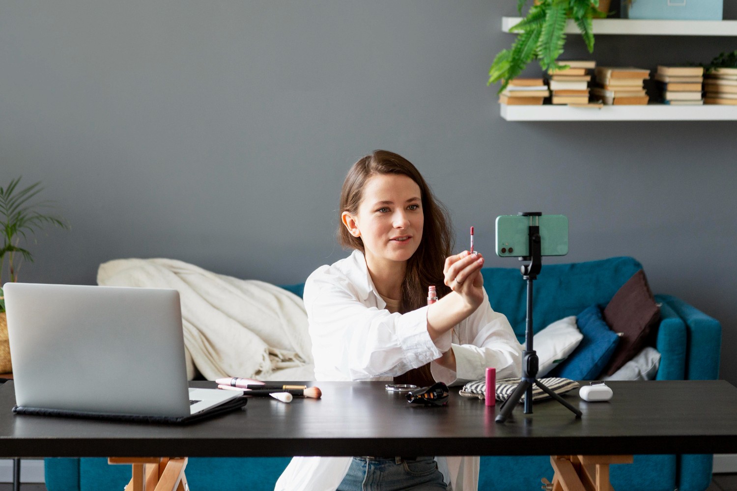 A woman seated at a table, working on a laptop with a camera positioned nearby.